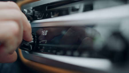 Male hand using knob for air conditioning at car. Close up unrecognizable person adjusting temperature in car. Closeup man hand increasing temperature on car dashboard at vehicle.の写真素材