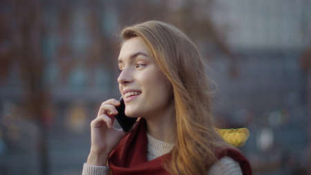 Closeup joyful woman speaking mobile phone on walk outdoors. Portrait of attractive girl enjoying conversation smartphone on city street. Natural beauty woman walking with cellphone outside.の写真素材