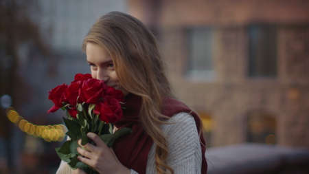 Portrait of cute hipster girl smelling bouquet of flowers outdoors. Closeup sweet woman holding floral bunch in hands outside. Smiling female person carrying roses on city street.の写真素材