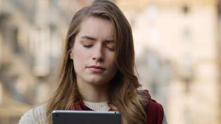 Portrait of focused hipster woman standing with tablet computer outdoors. Closeup thoughtful girl face looking tablet screen in urban background. Serious female person holding tablet on city street.の写真素材