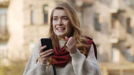 Portrait of cheerful woman getting great news on mobile phone outdoors. Closeup excited woman...