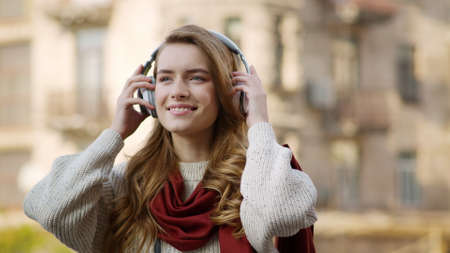Portrait of playful woman listening music via wireless headphones outside. Closeup cheerful hipster...