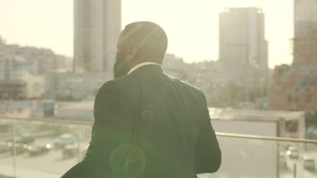 Joyful afro businessman in formal wear dancing at modern street. African business man enjoying victory on street. Portrait of male office worker having fun outdoors in slow motionの写真素材