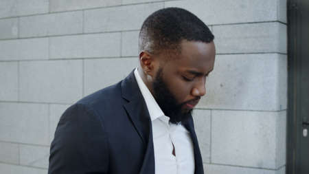 Closeup thoughtful businessman walking on city street. African american male employee looking down...