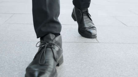 Low view unrecognizable businessman in black shoes going for job on sidewalk. Front view male worker walking on city road in slow motion. Closeup of business man legs walking on pavementの写真素材