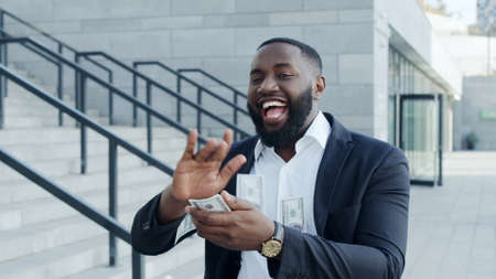 Close up crazy african businessman throwing money at city street. Excited afro male entrepreneur...