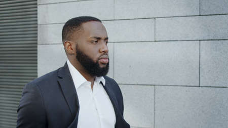 Portrait of serious businessman in suit walking on street. Afro male professional going for work outdoors in slow motion. Confident african business man taking walk around city.の写真素材