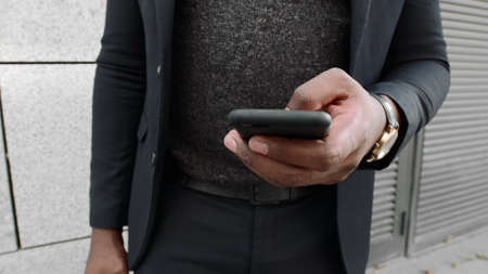 African businessman hands browsing internet on cellphone outdoors. Closeup male manager using smartphone on street. Business man in suit texting message on phone in slow motionの写真素材