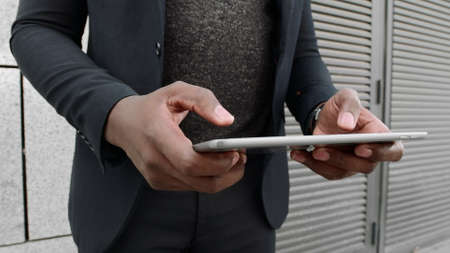 Low view african businessman in suit typing on digital tablet on city street. Business man hands...