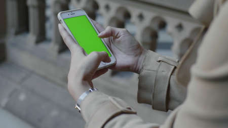 Unrecognizable student hands using smartphone with green screen in colonnade hallway. Close up young...