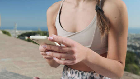 Closeup unrecognizable sportswoman using smartphone after outdoor workout. Woman hands typing on...