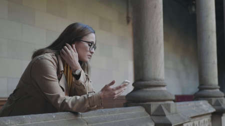 Portrait of upset student reading bad news on mobile phone in college building. Young woman standing in university hallway. Stressed businesswoman using smartphone outdoors in slow motionの写真素材