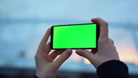 Closeup woman hands using smartphone with green screen outdoors. Unrecognizable girl taking picture on mobile phone. Unknown lady holding cellphone with chroma key in arms on streetの写真素材