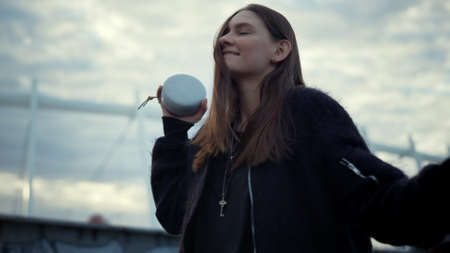Happy girl dancing with wireless speaker in hand. Closeup positive girl moving to music. Portrait of...