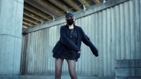Stylish girl dancing on city street. Fashion woman wearing face mask during street protest. Hipster woman showing fuck you sign. Young lady showing middle finger at camera outdoorsの写真素材
