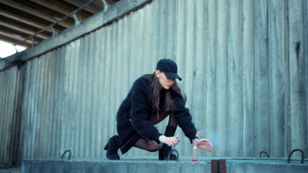 Fashion girl lighting smoke grenade on urban street. Serious woman in cap protesting with lighter outdoors. Attractive lady holding sparkling smoke bomb in hand. Hipster girl with smoke flare.の写真素材