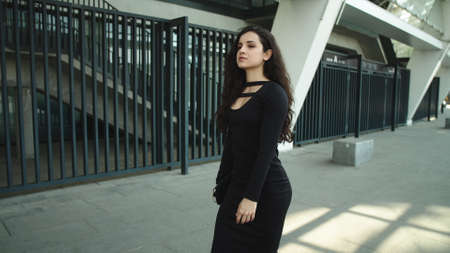 Close up sexy woman entrepreneur looking away at street. Confident business woman walking in black dress outdoors. Beautiful woman caring pouch at street.の写真素材