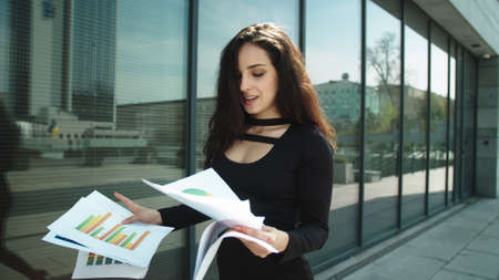 Close up business woman walking with documents at street. Successful woman entrepreneur throwing papers outside. Happy woman celebrating victory in black dress outdoors.の写真素材
