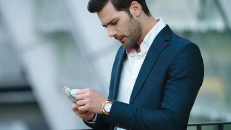 Portrait confident business man counting money at street. Successful businessman looking away with...