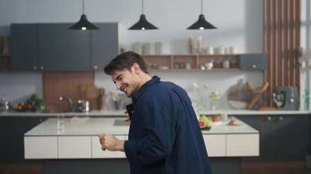 Portrait of attractive man enjoying dance on kitchen background. Sexy guy dancing with mobile phone in hand on domestic kitchen. Cheerful man smiling to camera indoors in slow motion.の写真素材