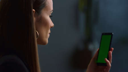 Focused businesswoman using mobile phone for video call at remote workplace. Female employee talking online on smartphone with green screen indoors. Business woman chatting on phone at home officeの写真素材