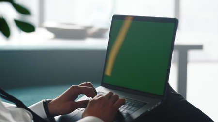 Closeup unrecognizable businessman typing on laptop with green screen. Male hands working on computer with chroma key at remote workplace. Unknown business man using keyboard on laptop at home officeの写真素材