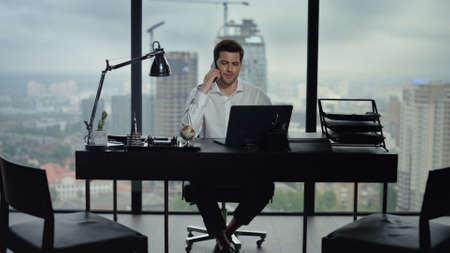 Smiling businessman talking smartphone at remote workplace. Male professional having conversation on...