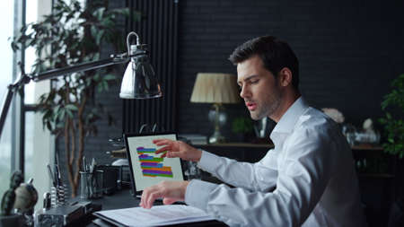 Focused businessman analyzing financial statistics on documents with graphs on laptop screen.