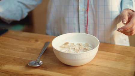 Woman hands pouring milk into cornflakes bowl on kitchen table. Pretty woman eating cereal at home...
