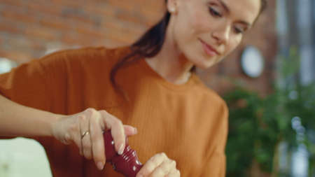 Portrait of attractive girl adding spices to healthy salad in kitchen. Closeup smiling woman seasoning food in kitchen table. Happy female brunette cooking mixed vegetables at home.の写真素材