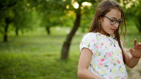 Happy teen girl making rhythmical movements in summer park. Smiling teenage girl dancing outside...