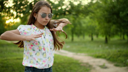 Concentrated teen making rhythmical movements in summer park. Serious teenage girl dancing outside. Stylish girl in sunglasses dancing rap outdoors in slow motion.の写真素材