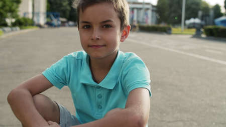 Portrait of cute boy sitting in amusement park. Close up smiling child spending time outdoors. Handsome teenager sitting on road outside.の写真素材