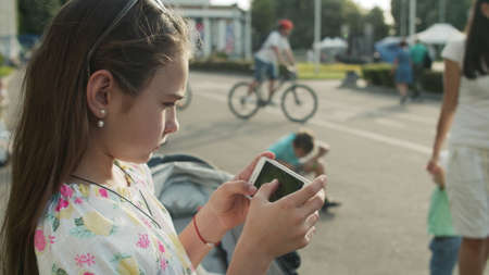 Close up serious girl playing mobile phone in amusement park. Concentrated teenager using smartphone outdoors. Cute teen girl holding phone outside.の写真素材