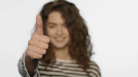 Portrait of happy girl showing thumbs up on white background. Young woman showing thumb up in studio. Close up of smiling model show thumb up. Happy girl show like gestureの写真素材