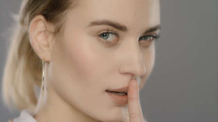 Young woman showing silence sign. Blonde girl putting finger on mouth in studio. Beautiful woman...