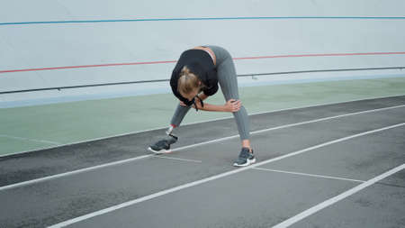 Female runner with prosthetic leg preparing for workout on sports track. Sporty woman stretching...