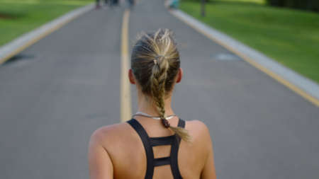 Overhead view female jogger training on running surface in park. Back view of young runner woman...
