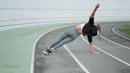 Back view disabled athlete standing in plank on hand at athletics track. Fit woman training at...