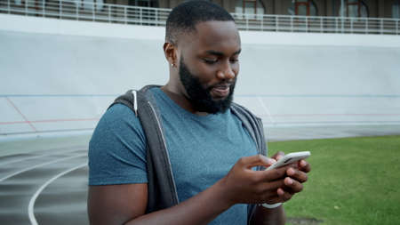 Closeup runner reading good news on smartphone at track. Portrait of handsome afro man using mobile...