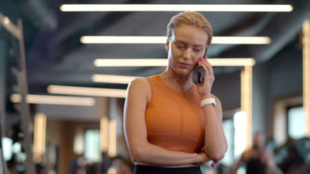 Curious athlete girl using mobile phone in fitness center. Portrait of smiling sportswoman having...