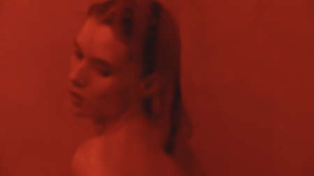 Portrait of sexy girl flirting in bathroom. Closeup wet woman cleaning mirror in bathroom in red light. Provocative woman looking at mirror in bath.の写真素材