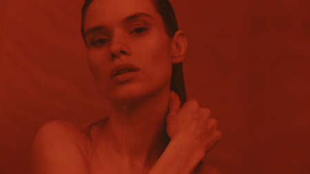 Close up of attractive woman taking shower in slow motion. Closeup nude girl posing for camera in bathroom. Provocative woman washing hair in bath in red light.の写真素材