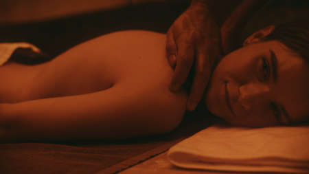 Closeup pretty woman having massage at luxury spa. Young woman getting body massage. Man hands massaging back at dark room. Portrait of relaxed girl in spa.の写真素材