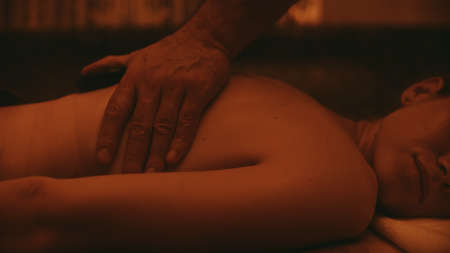 Close up of man hands making massage in slow motion. Closeup female body getting massage in spa center. Male professional massaging woman with hot stones. Woman relaxing with spa massage.の写真素材