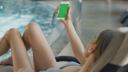 Close up of beautiful woman using phone with chroma key by pool at hotel. Sexy girl waving hand to...