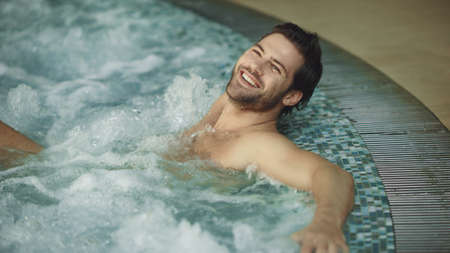 Smiling man relaxing in hot tub spa at luxury hotel.