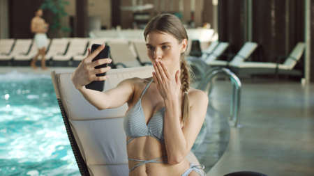 Portrait of young woman making self portrait on lounger near swimming pool. Closeup sexy girl making...