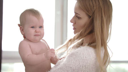 Sad baby on mom hands. Unhappy child pull hair of mother. Young mother holding infant kid on...