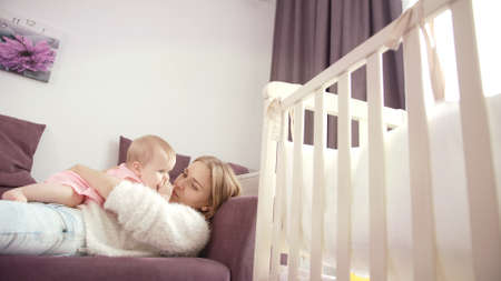 Mother with baby lying on sofa. Pretty woman lying on bed with kid. Mom hugging little child....